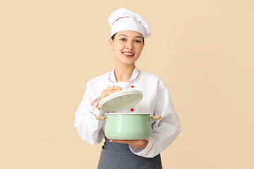 Female Asian chef with cooking pot on beige background