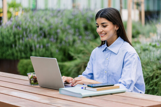 Happy student woman working on laptop outside at college campus. MBA education concept