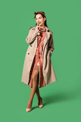 Portrait of beautiful pin-up woman in coat on green background