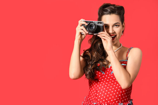 Portrait of beautiful pin-up woman with photo camera on red background