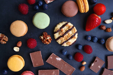 Macarons, chocolate, cookies, berries and various nuts on dark blue background. Top view.