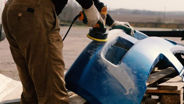 man repairing bumper, sanding paint for painting, repairing cracked bumper.