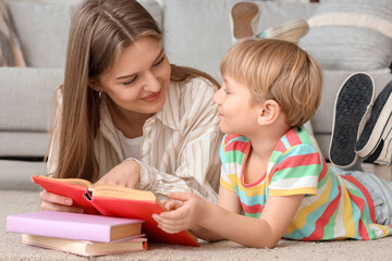 Little boy and his mother reading book while lying on floor at home
