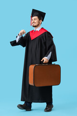 Male graduate student with keys and suitcase walking on blue background