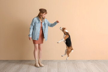 Young woman in casual attire playing with cute beagle dog on beige background