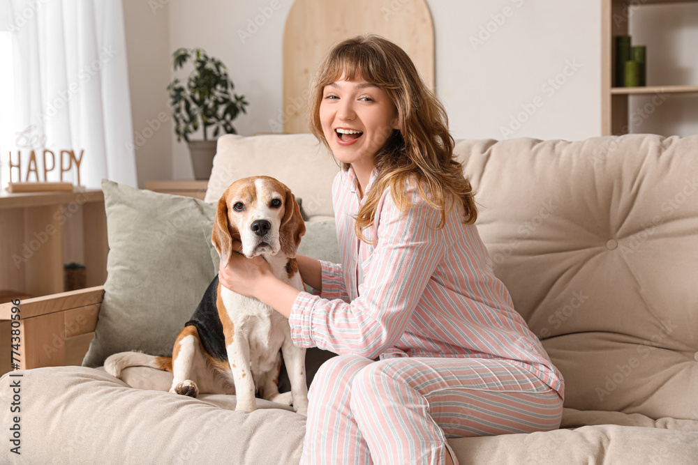 Sticker Young woman with cute beagle dog sitting on sofa at home