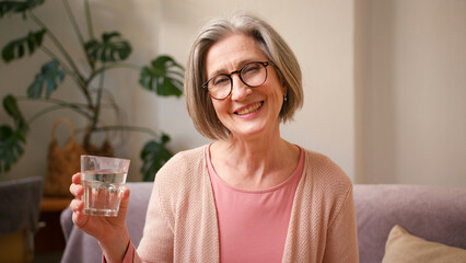 Mature old 60s woman, older middle aged female customer holding glass of water and drinking it on...