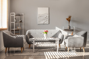 Interior of light living room with sofa, armchairs and tulips on table