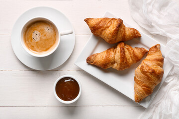Plate with tasty croissants and cup of coffee on white wooden background