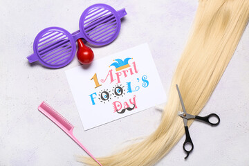 Card with text  APRIL FOOL'S DAY, hair strand and hairdresser's supplies on light background
