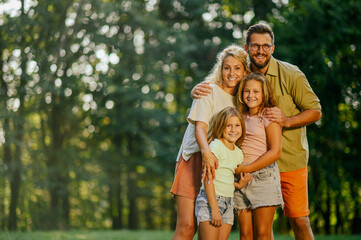 Fototapeta premium A joyful family is standing and hugging in nature near forest.
