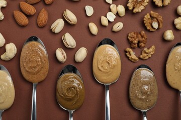 Fototapeta na wymiar Tasty nut butters in spoons and raw nuts on brown table, flat lay