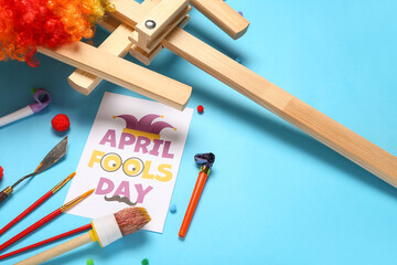 Card with text APRIL FOOLS DAY, artist's tools and party whistles on color background