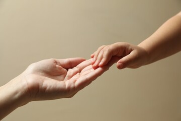 Mother and child holding hands on beige background, closeup