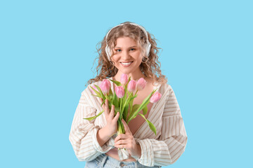 Pretty young woman in headphones with bouquet of beautiful tulips on blue background