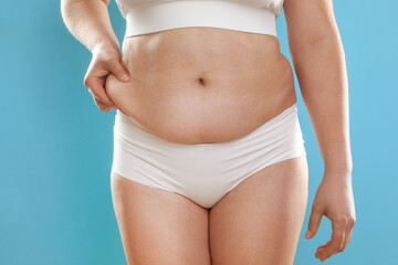 Woman touching belly fat on light blue background, closeup. Overweight problem