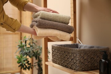 Woman putting towels into storage basket indoors, closeup