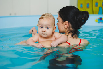 Trainer teaches baby to swim, swimming pool for children. Child development.