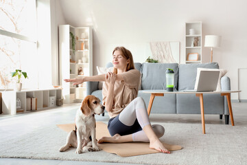 Sporty young woman with cute Beagle dog doing yoga at home