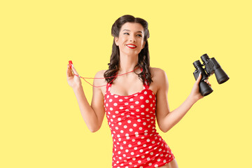 Beautiful pin-up lifeguard with whistle and binoculars on yellow background