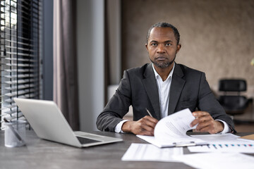 Professional male executive engaged in paperwork at his desk with a laptop in an office setting.