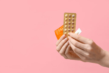 Female hands with birth control pills, vaginal suppositories and condom on pink background