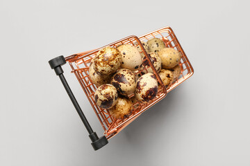Shopping cart with fresh quail eggs on grey background
