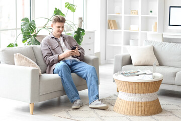 Young man using mobile phone on sofa at home