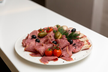 Meat delicatessen plate arranged with cherry tomato, black and green olives and capers.