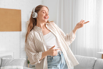 Happy young woman in headphones dancing at home