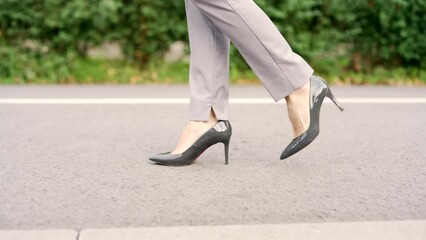 Close up. Female legs in high heels of black shoes walking in the urban street along park alley. Stylish woman in gray pants walks on the road. Feet of an adult businesswoman in footwear going in park