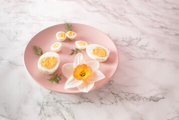 Boiled chicken and quail eggs and narcissus on pink plate on kitchen marble background. Healthy raw food concept