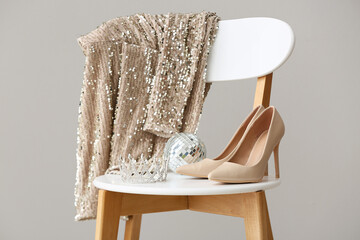 Prom dress with female shoes, crown and disco ball on chair against white background