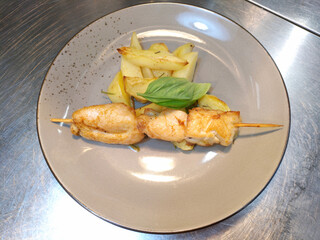 chicken fillet skewers and potato wedges with a sprig of basil on a white plate. delicious and...