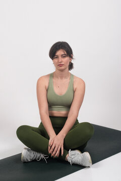 Fitness woman in sportswear sitting on a yoga mat against a white background, looking relaxed and contemplative.