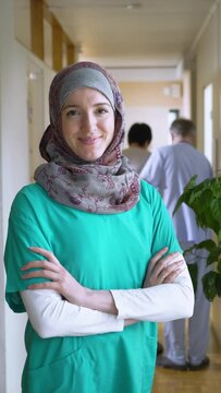 A female medical doctor or nurse wearing hijab standing proudly and smiles for the camera. Confident Muslim female doctor standing inside hospital