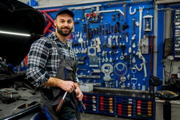 A proud Caucasian mechanic showcases workshop ownership, skillfully holding tools, capturing the...