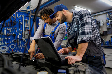 Dynamic duo at work: Mechanic colleagues dive into car diagnostics with a computer, complemented by a handheld lamp for precision, ensuring thorough problem-solving.