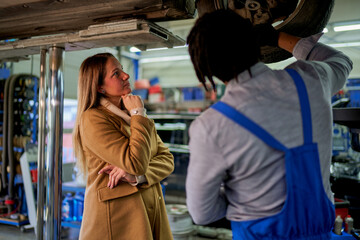 Fototapeta premium In the workshop, a woman client and a mechanic with tools, discussing car troubles. A scene of communication and guidance.