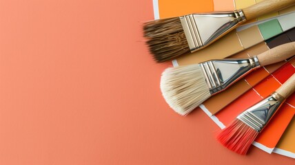 Paintbrushes rest on a coral background with palette of color swatches - obrazy, fototapety, plakaty