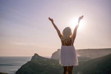 A woman is standing on a hill overlooking a body of water. She is wearing a white dress and she is happy.
