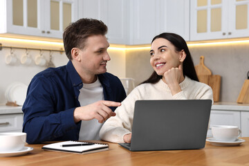 Happy couple using laptop at wooden table in kitchen