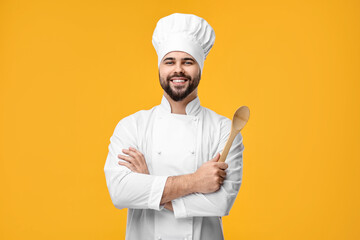 Happy young chef in uniform holding wooden spoon on orange background