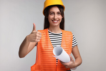 Architect in hard hat with draft showing thumbs up on light grey background
