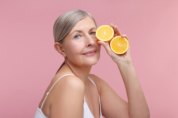 Beautiful woman with halves of orange rich in vitamin C on pink background