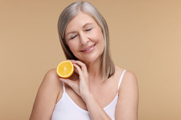 Beautiful woman with half of orange rich in vitamin C on beige background