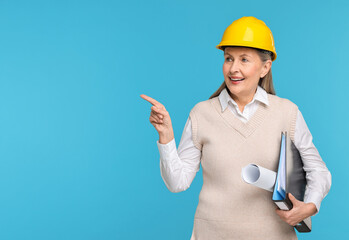 Architect in hard hat with draft and folder pointing at something on light blue background, space...