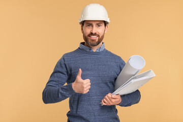Architect in hard hat with draft and folder showing thumbs up on beige background