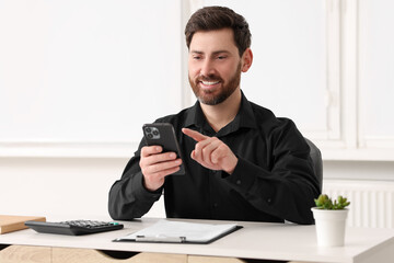 Smiling man using smartphone at table in office