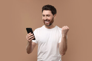 Happy man with smartphone on light brown background